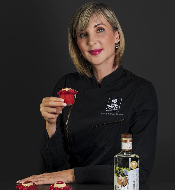 Photographie sur fond noir de Cécile Moritel tenant la pâtisserie au Gin, préparé avec du Sober Spirits gin 0.0% d'alcool et de sucre présent à côté d'elle.